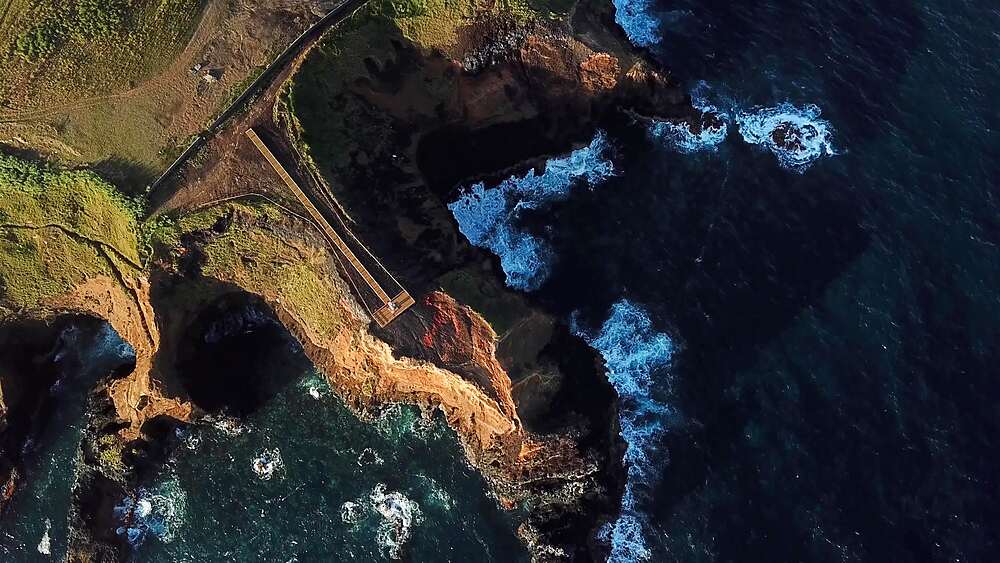 Top down drift over sea caves carved into a basalt headland, Farolim dos Fenais da Ajuda, Sao Miguel, Azores