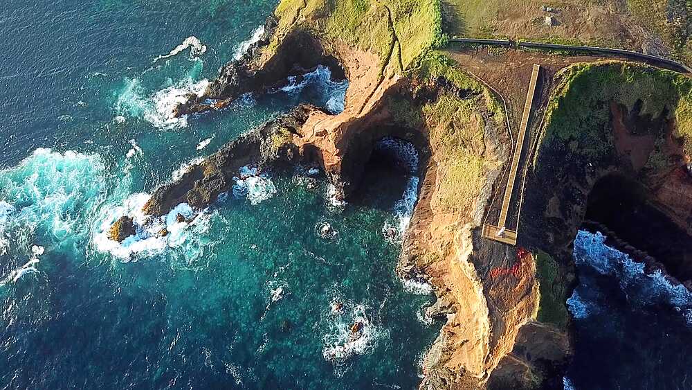 Drone orbit reveals three sea cave arches beneath a coastal headland, Farolim dos Fenais da Ajuda, Sao Miguel, Azores