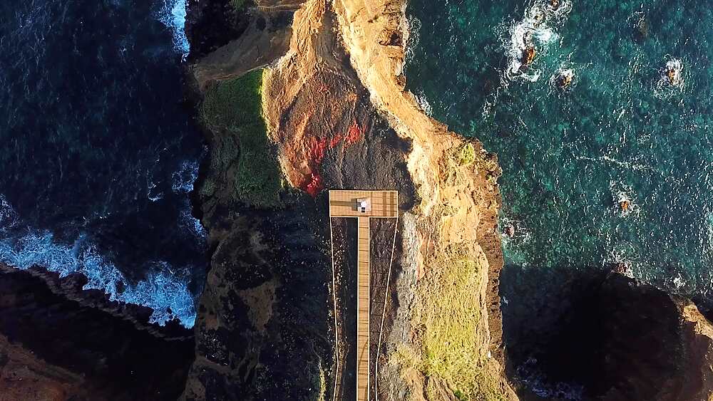 Rising drone unveils the full boardwalk leading to Farolim dos Fenais da Ajuda lighthouse, Sao Miguel, Azores