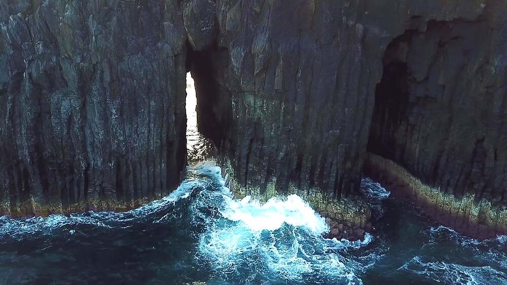 Silent glide through a slot between columnar basalt cliffs with surging Atlantic surf, Sao Miguel, Azores