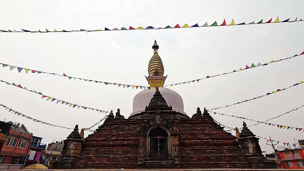 Chilancho Stupa frontal wide shot, white dome with Buddha eyes and gold spire, colourful prayer flags, Kirtipur, Nepal