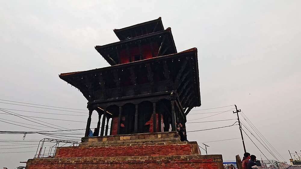 Bagh Bhairab Temple three-tiered Newari pagoda low-angle, dark carved wood and brick plinth against grey sky, Kirtipur Nepal