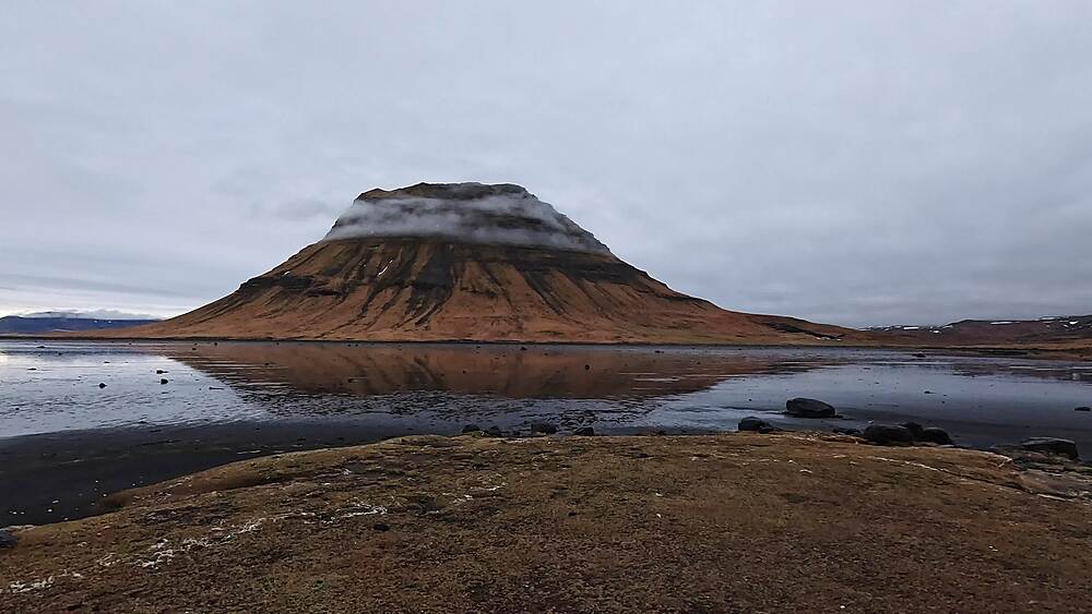 Kirkjufell flat-topped peak with low cloud reflected in still tidal flats at dusk, Grundarfjordur, Iceland