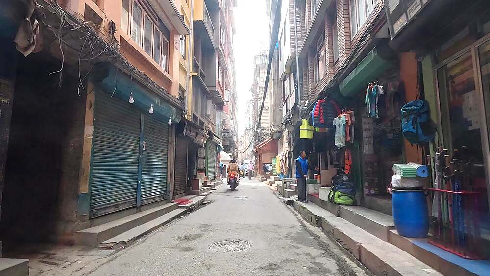 Rearward car-window view down a narrow Thamel lane past a small shrine, Kathmandu, Nepal