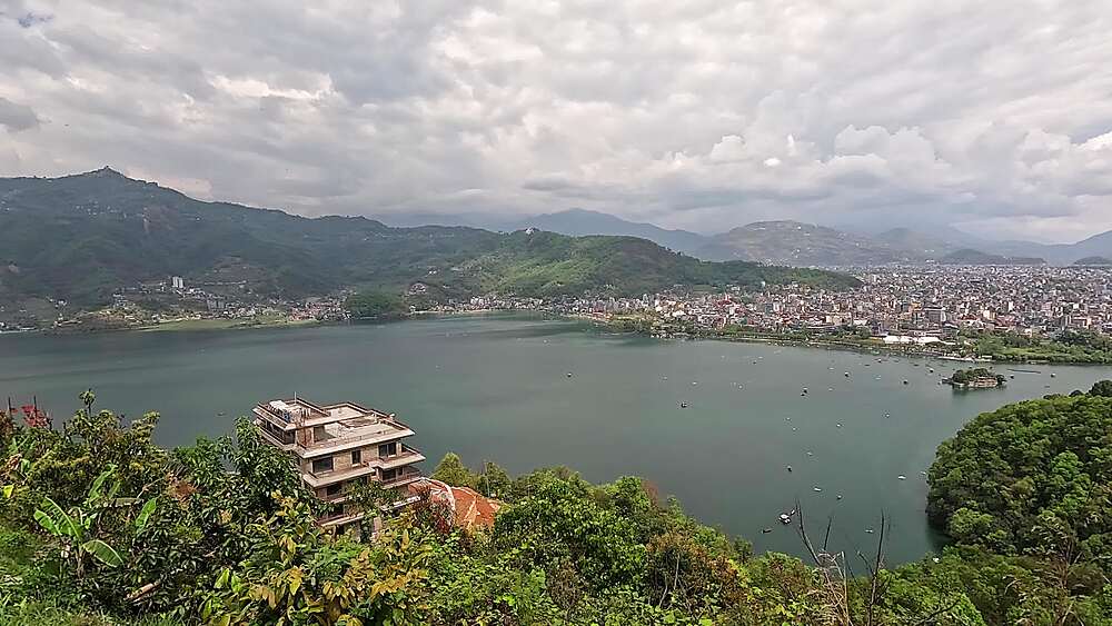 Hillside pan across Phewa Lake toward the dense skyline of Pokhara, Nepal