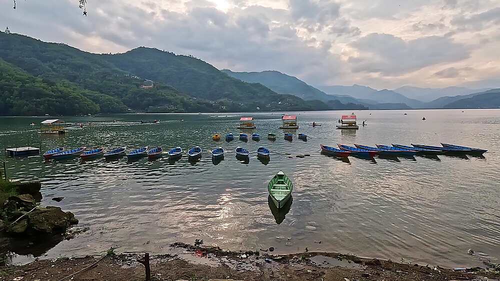 Slow pan over moored wooden boats on calm Phewa Lake at dusk, Pokhara, Nepal