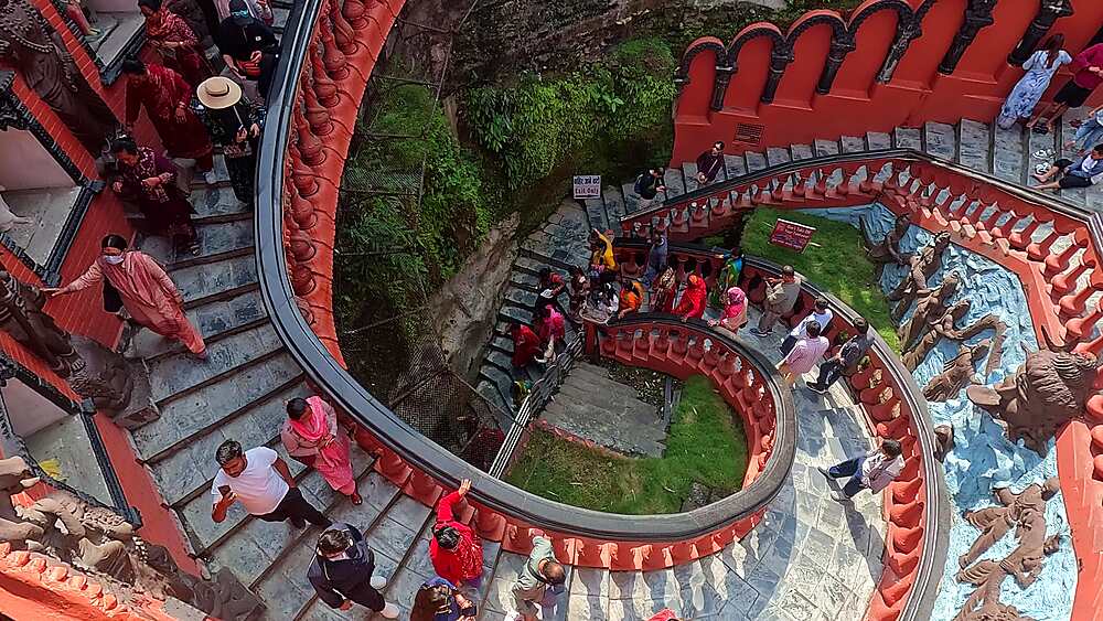 Downward pan over the descending red spiral staircase and relief panels at Gupteshwor Mahadev Cave, Pokhara, Nepal