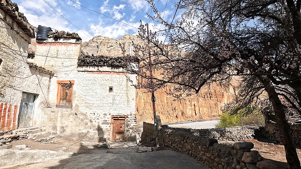 Forward walking POV down a narrow alley past a whitewashed house with carved window, Chhusang village, Upper Mustang, Nepal