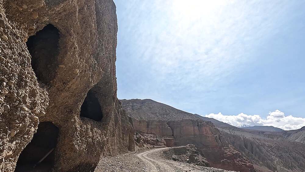 Driving POV along a narrow mountain track carved into a cliff above a vast arid valley, Upper Mustang, Nepal