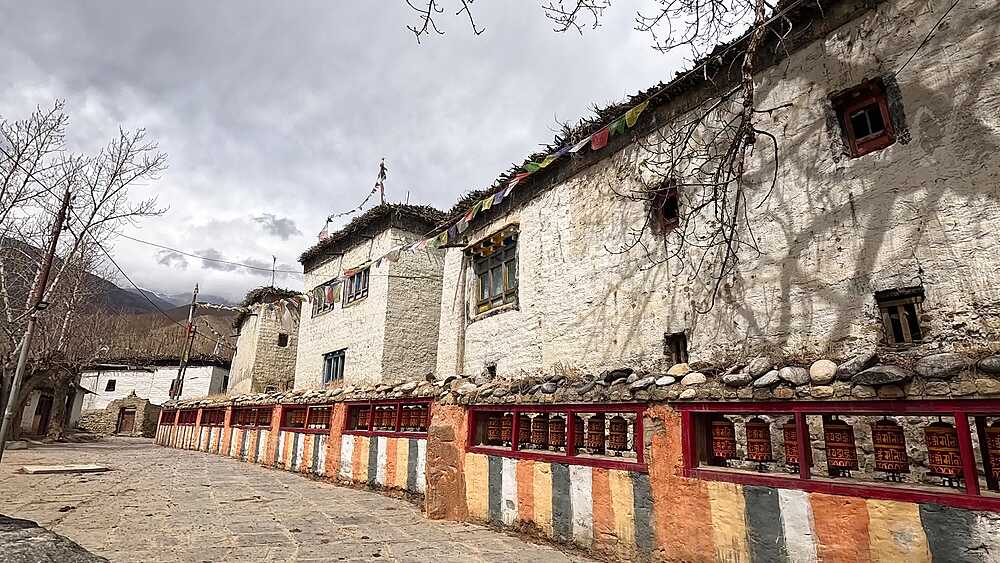 long wall of red prayer wheels beside whitewashed houses, Ghami village, Upper Mustang, Nepal