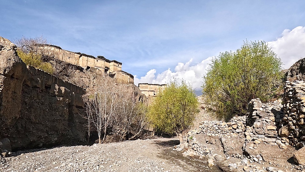 Dolly in along riverbed with dry mud brick houses on eroded cliffs. Tetang Village. Upper Mustang, Nepal