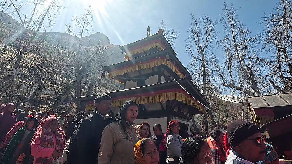 Low angle shot of golden Mukti Narayan Temple with sun flare and crowds, Muktinath, Nepal