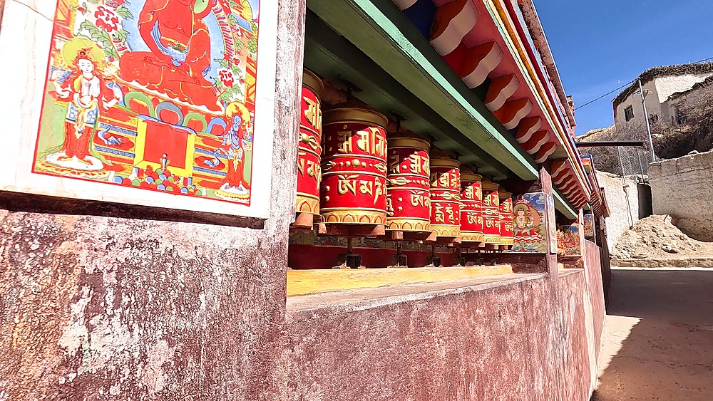 Row red gold prayer wheels painted deity panels Lo Garphu Upper Mustang Nepal
