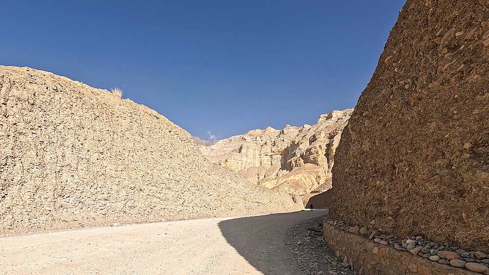 Hiker on Chele-Lomanthang Road through narrow canyon cut between pale sandstone walls Nepal