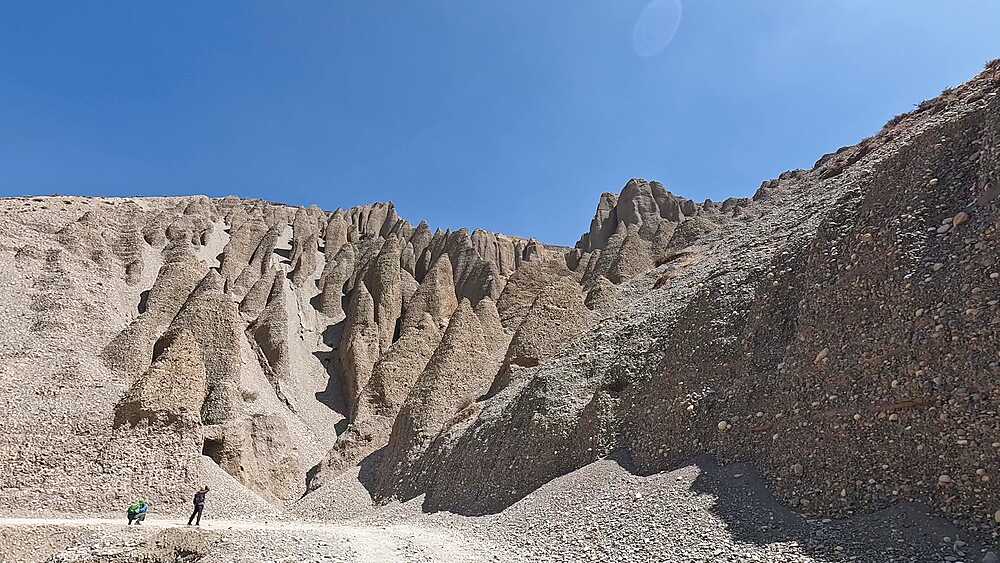Trekkers dwarfed by towering earth pyramid hoodoo formations, Upper Mustang geological landscape Nepal