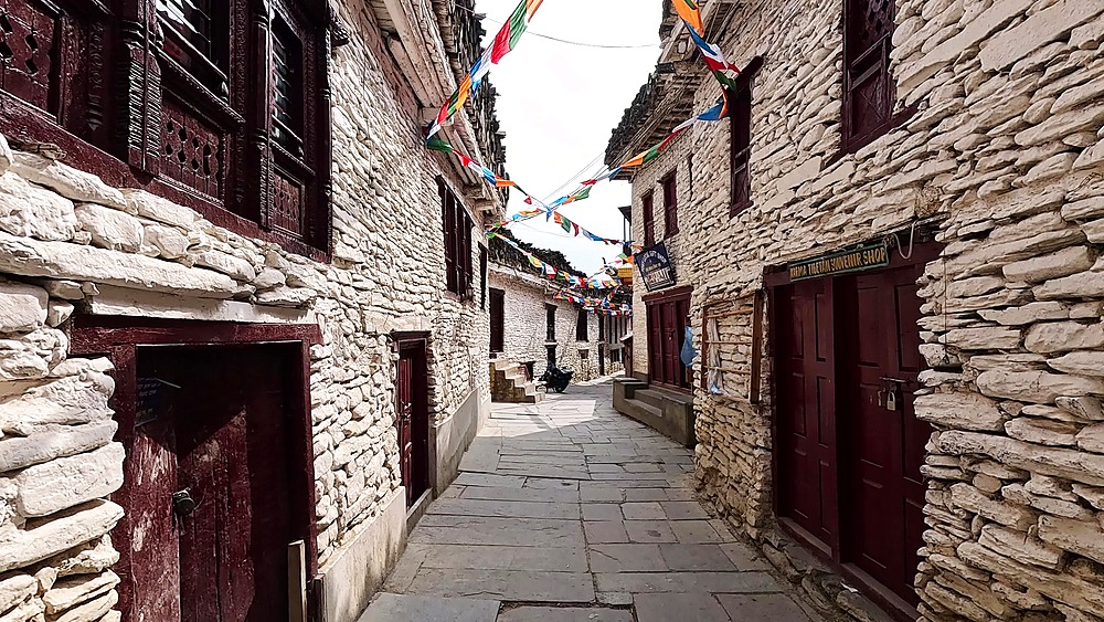 Narrow stone alley, white buildings, prayer flags, Marpha village traditional Mustang
