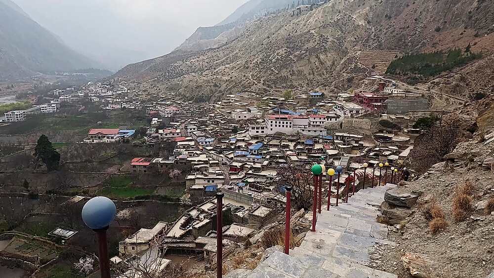 Elevated Marpha village view following stone staircase, prayer flag decorations, valley backdrop Mustang Nepal