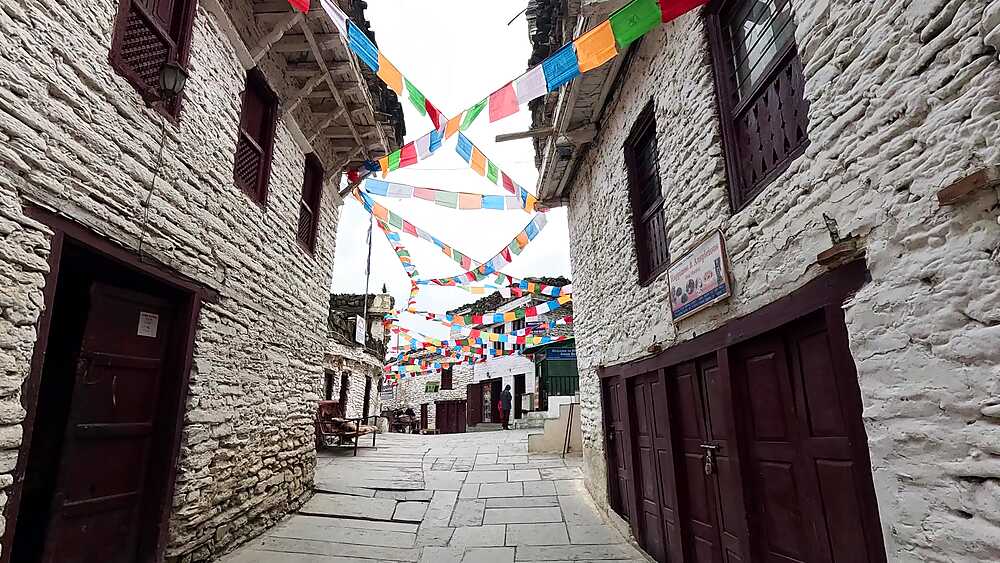 Village street people traditional red dress, stone buildings, prayer flags Marpha