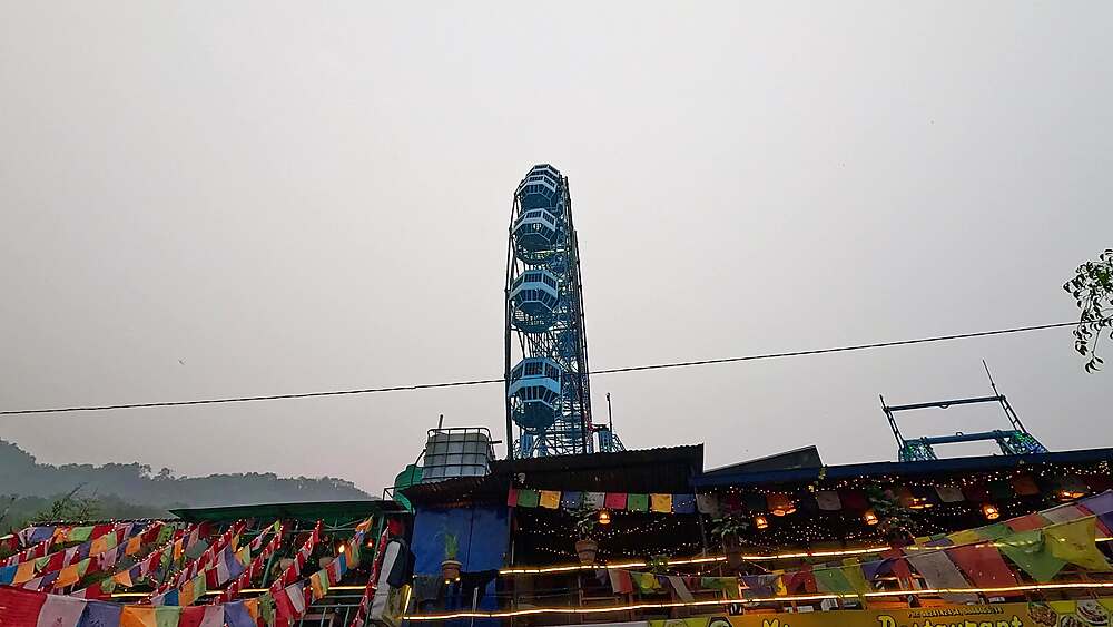 Tall ferris wheel silhouette against twilight sky, prayer flags, dusk lights amusement park Phewa Lake
