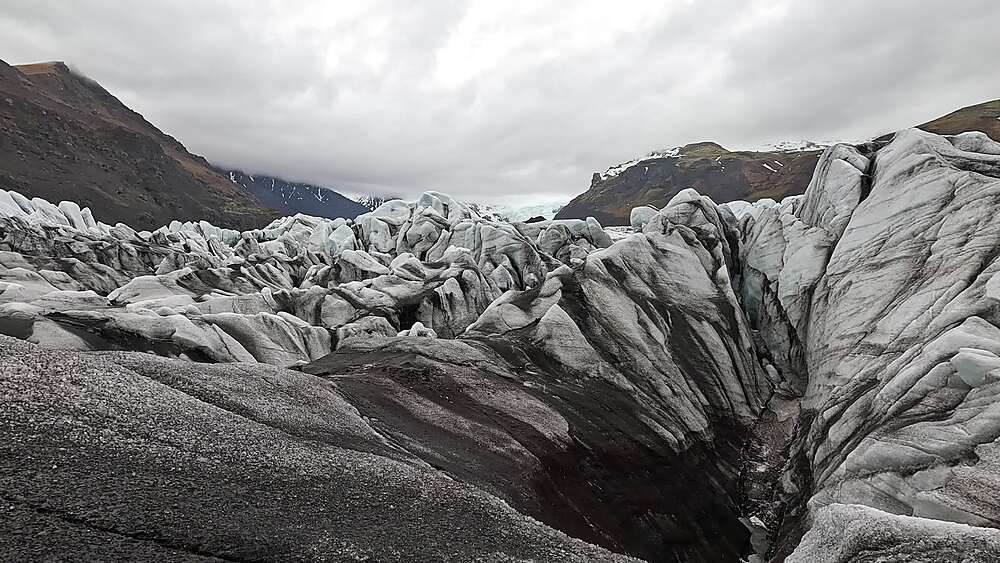 Svinafellsjokull wide crevasse field with deep V-shaped channel and glacier flowing right, Iceland