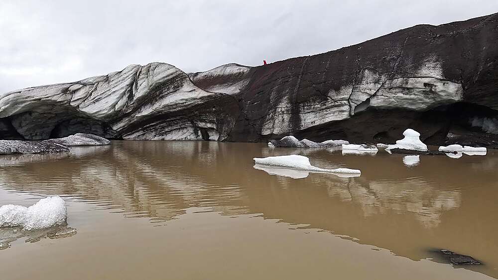 Svinafellsjokull lagoon close-up, ice chunks floating in silty meltwater near ash-streaked glacier snout cave
