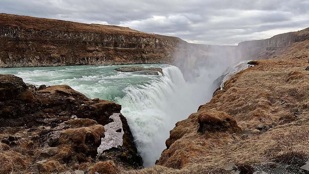 Gullfoss lower tier close-up, glacial green water plunging into basalt gorge with ice on rocks, Iceland