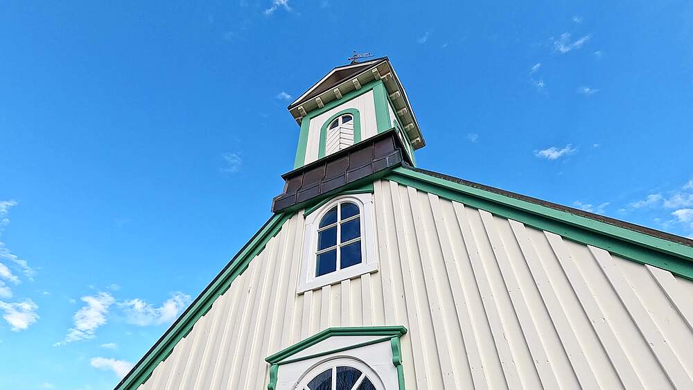 Low-angle upward shot of Thingvallakirkja historic church tower with cream and green facade against blue sky, Iceland