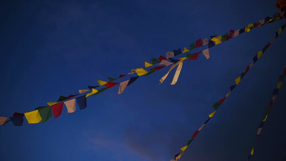 Strings of colourful Tibetan Buddhist prayer flags flutter against a deep blue dusk sky, Kathmandu, Nepal