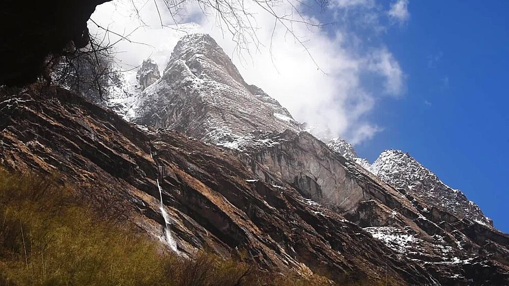 Dramatic rocky slopes with a thin waterfall below the peaks of the Annapurna range, Nepal