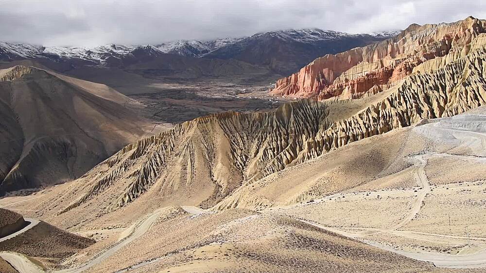 Pan over a mountain pass road revealing the red cliffs of Dhakmar and eroded badland canyons, Upper Mustang, Nepal