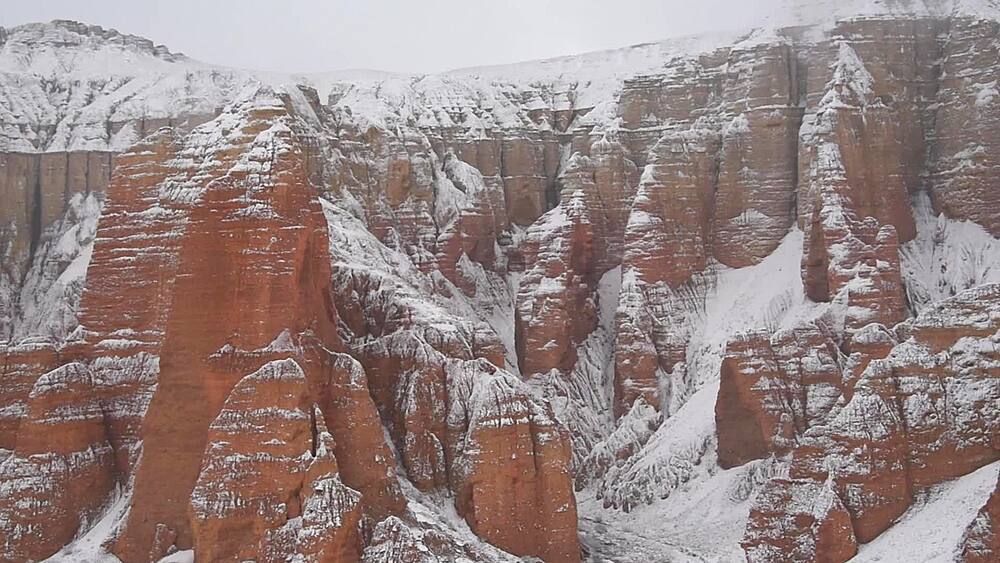 Pan across snow-dusted red sandstone cliffs and eroded hoodoos at Dhakmar, Upper Mustang, Nepal
