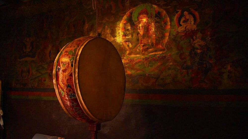 Ritual drum hanging before a gilded deity mural in the dim interior of Luri Gompa cave monastery, Yara, Upper Mustang, Nepal
