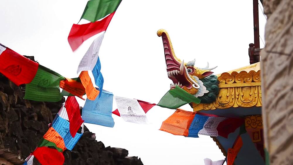 Carved dragon roof finial and Buddhist prayer flags against bright sky in Marpha