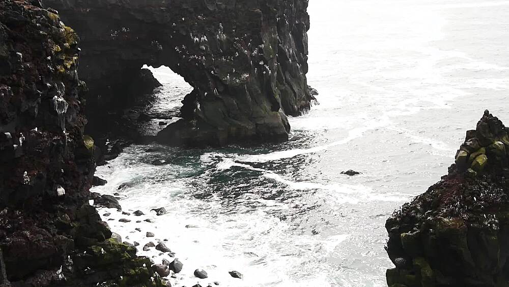 Static shot of sea arch and cliffs at Londrangar with waves surging below nesting seabirds, Snaefellsnes Peninsula