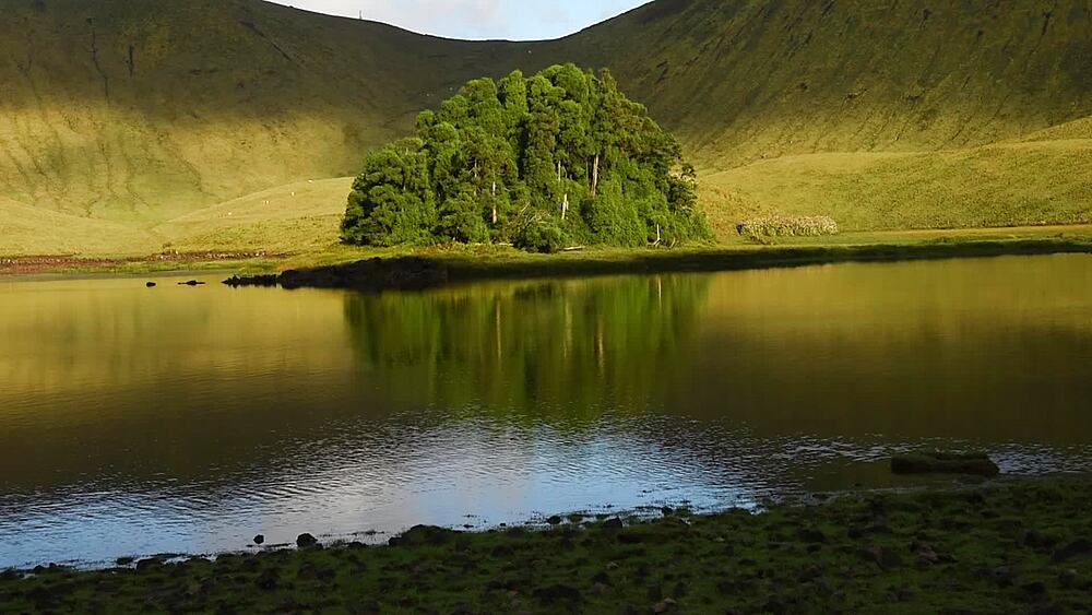 Wooded islet mirrored in the still Caldeirao lagoon at golden hour, Corvo Island, Western Group, Azores