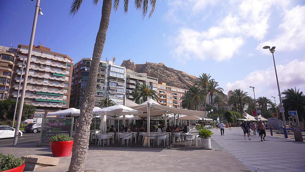 View of people at cafe on Explanada of Spain and Castillo de Santa Barbara in background on a sunny day, Alicante, Costa Blanca, Spain, Europe