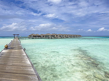Bungalows on a wooden pier extend into clear turquoise water in the Maldives
