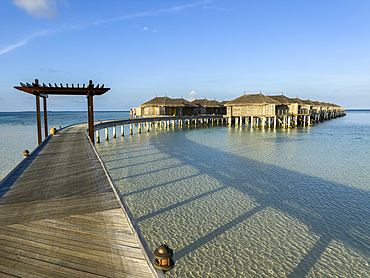 Bungalows at a tropical resort in the Maldives with wooden walkways and clear water under blue skies