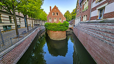 Small channel surrounded by buildings and green plants in Amiens offers a view of the waterway and architecture during the day