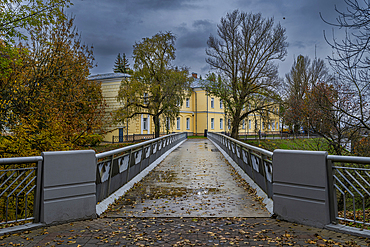Visitors walk on a bridge toward a historic building in a park on a cloudy day in Gomel, Belarus