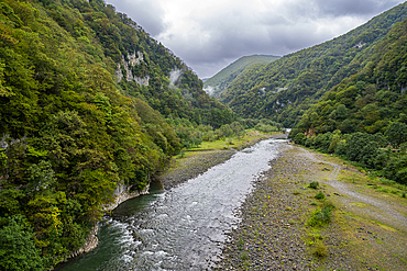 Lupshara river flows through a green valley in Ritsa Relict National Park with rocky banks and forested hills in Russia