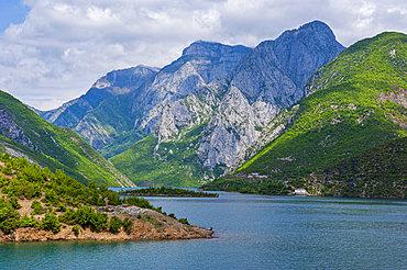 Koman water reservoir shows mountains and clear water under a cloudy sky in Albania during springtime