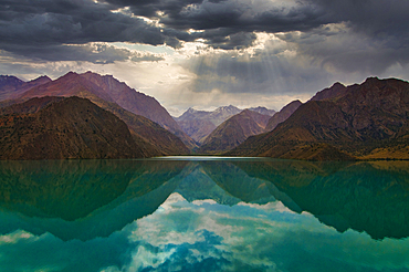Turquoise water reflects mountains under a cloudy sky in Alexanderlake, Iskanderkul, Tajikistan