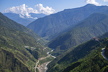 Views of gorge in eastern Bhutan with winding road and lush hills in the distance during a clear day
