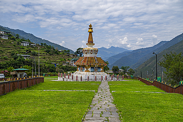 Stupa stands in Trashigang surrounded by grass and mountains in Eastern Bhutan with cloudy sky