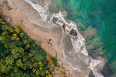 Shipwreck on beach in Manzanillo with crashing waves and rainforest scenery in Costa Rica