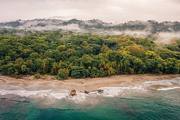 Shipwreck on a beach in Manzanillo in Costa Rica with rainforest and mist behind at sunrise