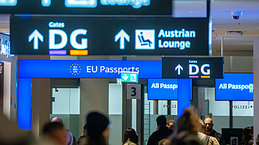 Travelers walk through Vienna International Airport, Austria with signs pointing to gates for EU and All passports