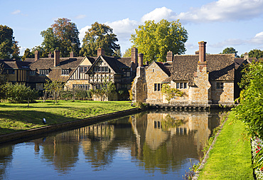 Cottages reflect in moat at Tudor Village near Hever Castle, Edenbridge, Kent, England, during clear weather