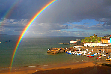 Bright rainbow over Tenby Harbour with boats and buildings by the shore in Pembrokeshire, Wales, during changing weather conditions